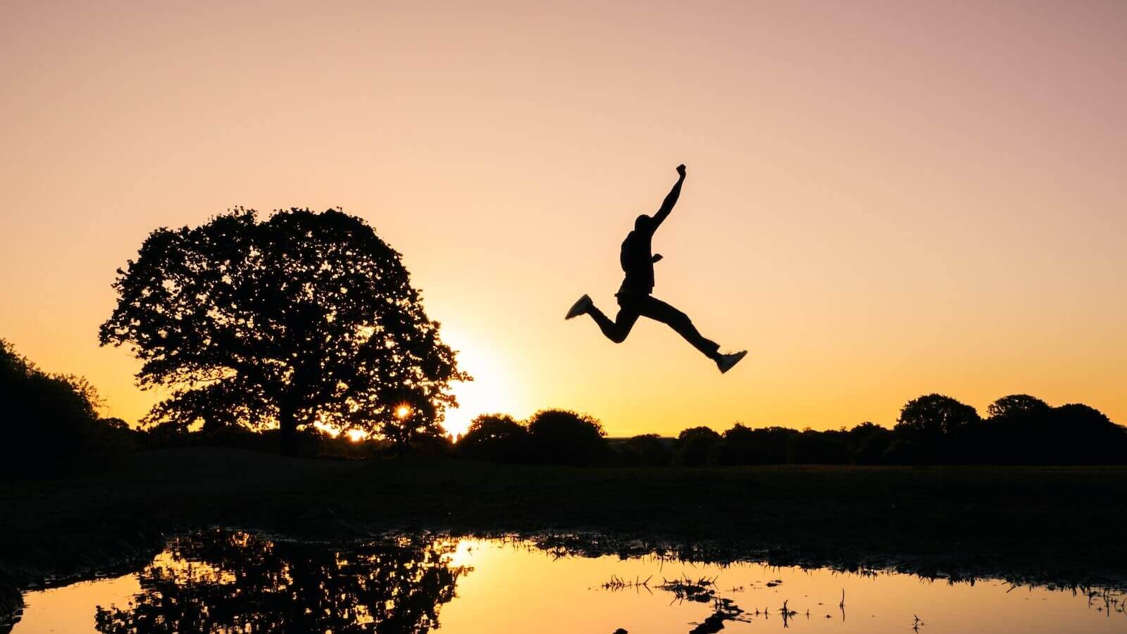 silhouette photo of man jumping on body of water during golden hour